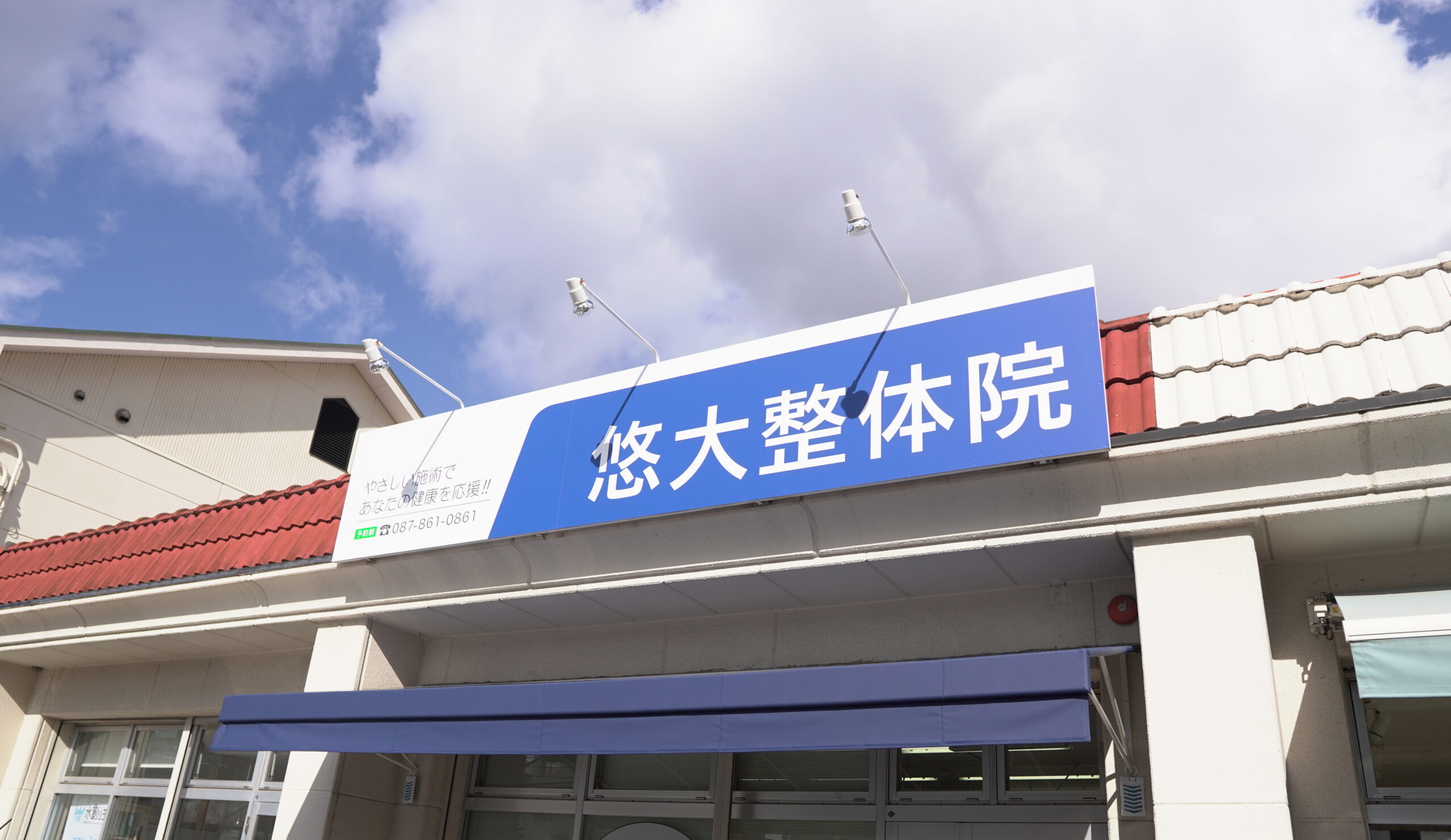 入り口の上に「悠大整体院」と書かれた青と白の看板が掲げられた香川県高松市の整体院。.