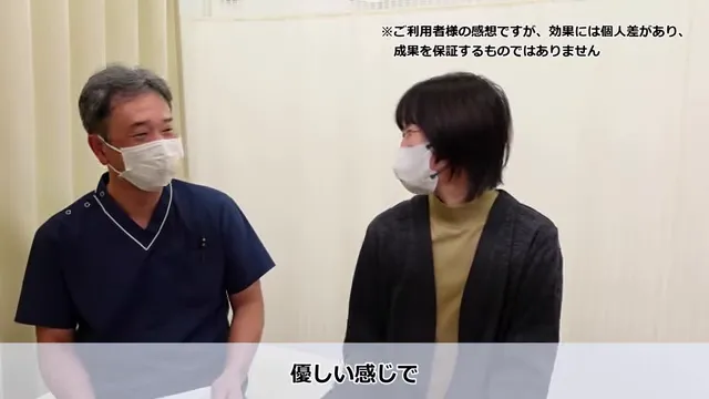 長年の肩こりと繰り返すめまいが根本改善したKさんの声 ソフトな施術でリラックスするKさん。マスク姿の2人が室内で座って話している。一人は濃い色の医療用スクラブ、もう一人はセーターとジャケットを着ている。彼らの上下に日本語の文字が見える。