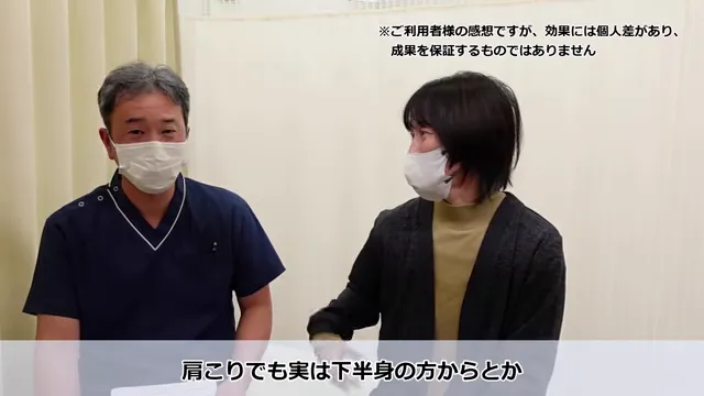 長年の肩こりと繰り返すめまいが根本改善したKさんの声 下半身から体全体を整えるアプローチの説明場面。濃い色の医療用スクラブ姿の男性とカジュアルな服装の女性が、白いマスクをつけて室内で並んで座っている。画像の右上と下には日本語のテキストが表示されている。